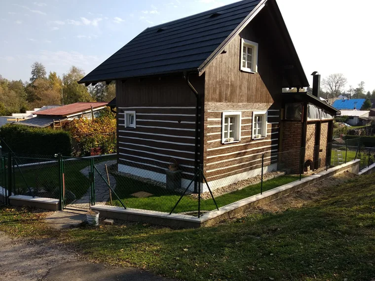 Roubená chalupa s novou tmavou střešní krytinou a okapy
